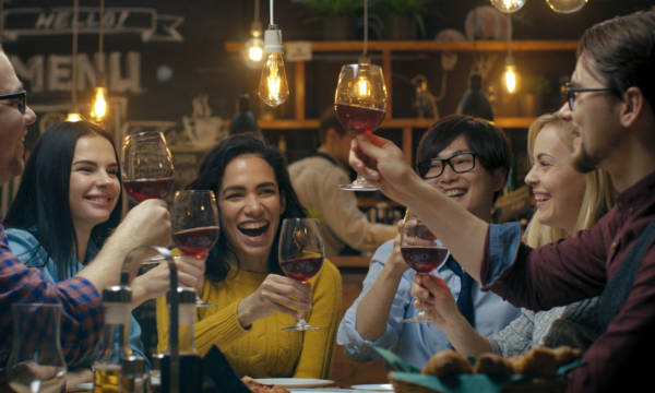 Diverse Group of Friends Celebrate with a Toast and Clink Raised Wine Glasses in Celebration. Beautiful Young People Have Fun in the Stylish Bar/ Restaurant.