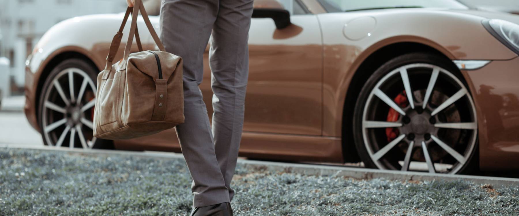 Cool man beautiful model outdoors, city style fashion. A handsome man model walking in the city center next to some cars. urban setting. The young boy as trendy, modern clothing with bag.